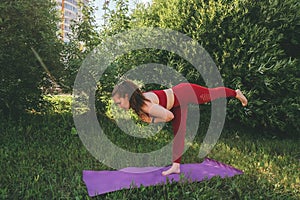 Young beautiful woman in red leggings and a top practicing yoga in a city park