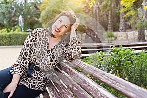 Young beautiful woman with red lips smiling happy sitting on a bench at garden