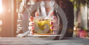 Young beautiful woman with red manicure drinking tea with herbs and lemon in cafe. Close up.
