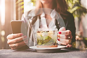 Young beautiful woman with red manicure drinking tea with herbs and lemon in cafe. Close up.