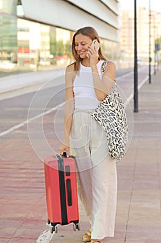 young beautiful woman with red suitcase calling smartphone while waiting for a taxi cab in the city. stylish smiling