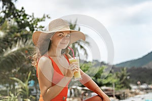 Young beautiful woman in a red swimsuit and a straw hat enjoying summer vacation, beach relax, summer in tropics