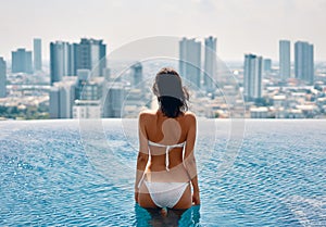 Young beautiful woman relax in swimming pool on rooftop and enjoy cityscape