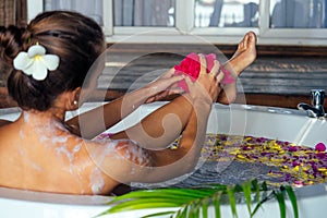 Young beautiful woman relaxing in bath with foam and tropical flowers petals,tropical flowers petals in eco hotel Bali