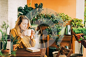 Young beautiful woman relaxing on cozy balcony, reading a book