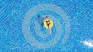 Young beautiful woman is relaxing in swimming pool with rubber yellow ring.