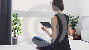 Young beautiful woman resting at home using digital tablet computer. Happy girl reading or shopping online.