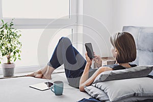Young beautiful woman resting at home using smart phone. Happy girl texting on her mobile phone online.