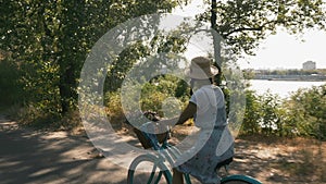 Young beautiful woman is riding bicycle at sunset, slow motion. Girl cyclist is cycling vintage retro bike on sunny road along riv