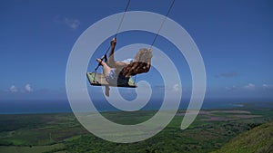 Young beautiful woman on the rope swing with sea and sky background in slow motion. Concept of Vacation and travel