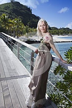 The young beautiful woman with a rose on a wooden path at the sea, tropics. Tahiti