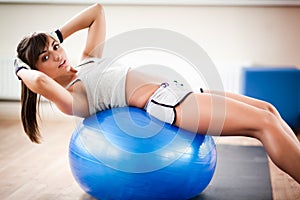 Young beautiful woman in sexy sportswear doing workout on blue fitness ball and looking at camera in gym