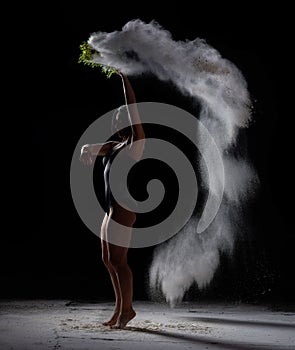 Young beautiful woman with short black hair dances on a dark background, holding a sieve with flour