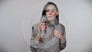 Young beautiful woman with short brown hair drinking from bottle with water and smiling, white background