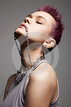 Young beautiful woman with short color hair and chain necklace in her mouth