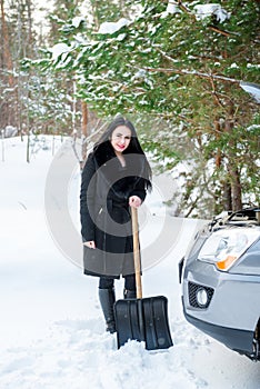 Young beautiful woman shoveling and removing snow from her car,