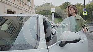 A young beautiful woman sit into her white premium car with a smartphone