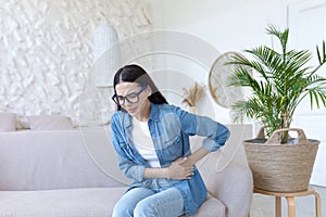 A young beautiful woman sits on the couch at home, sick, has severe pain in her stomach and side.