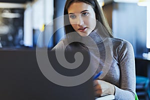 Young beautiful woman sits at a table in a cafe and uses a computer for telecommuting.