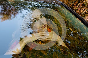 A young, beautiful woman sits at the wheel of the car and dreamingly watched through the glare of the front windshield.