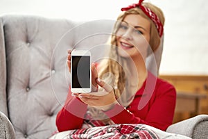 Young beautiful woman sitting in an armchair with a phone wrapped in a blanket during Christmas time