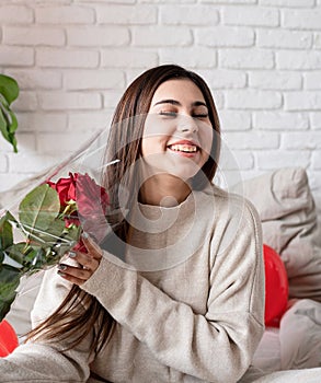 Young beautiful woman sitting in the bed celebrating valentine day holding red roses