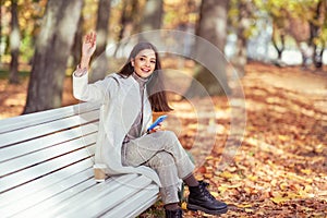 A young beautiful woman is sitting on a bench in an autumn park