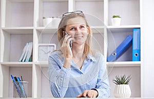 Young beautiful woman sitting in a chair and talking on the phone at her working place.