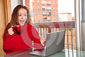 Young beautiful woman sitting with cup of coffee or tea and laptop computer