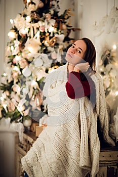Young beautiful woman with sitting home holding cup of hot coffee wearing knitted warm sweater. Christmas tree