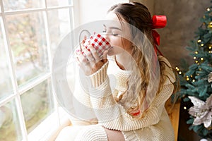 Young beautiful woman sitting home by the window with cup of tea. Christmas holiday