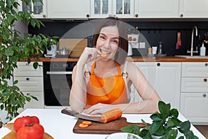 Young beautiful woman sitting at kitchen background while cutting vegetables