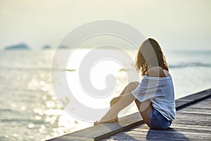 Young beautiful woman sitting on the pier enjoying sunset