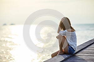 Young beautiful woman sitting on the pier enjoying sunset