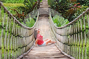 Young beautiful woman is sitting on suspension bridge in the tropic forest.