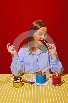 Young beautiful woman sitting at table and eating canned meat, drinking tomato juice against red background. Quirky food