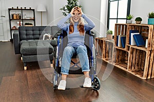 Young beautiful woman sitting on wheelchair at home doing ok gesture like binoculars sticking tongue out, eyes looking through