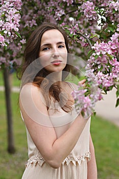 A young beautiful woman with a slight smile touches a blooming branch of an Apple tree