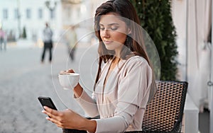 Young beautiful woman with smartphone sitting in the street cafe with coffee. Concept meeting, working, freelance