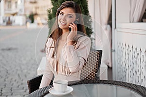 Young beautiful woman with smartphone sitting in the street cafe with coffee. Concept meeting, working, freelance