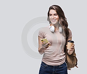 Young beautiful woman with smartphone studio portrait, smiling student girl going on travel holding coffee cup and mobile phone