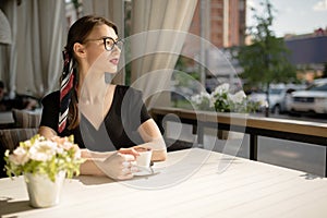 Young beautiful woman with a smile sits on the street and drinks coffee. Summer bright cafe