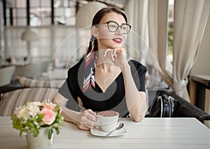 Young beautiful woman with a smile sits on the street and drinks coffee. Summer bright cafe