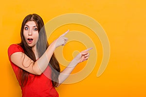A young, beautiful woman smiles and points a finger to the side. Studio photo on a yellow background.