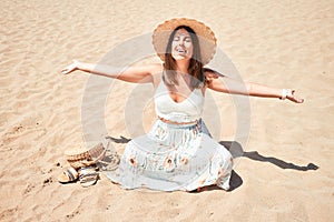 Young beautiful woman smiling happy enjoying summer vacation at the beach sitting on the sun sunbathing with open arms