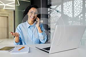 Young beautiful woman smiling and looking at camera, talking on the phone, businesswoman at workplace inside office
