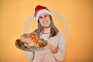 Young beautiful woman smiling proud holding thanksgiving turkey chicken on a tray wearing santa claus hat