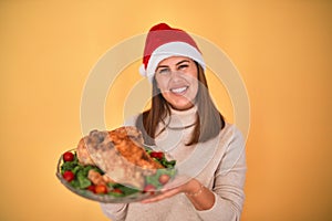 Young beautiful woman smiling proud holding thanksgiving turkey chicken on a tray wearing santa claus hat