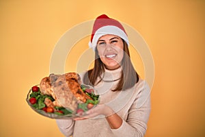 Young beautiful woman smiling proud holding thanksgiving turkey chicken on a tray wearing santa claus hat