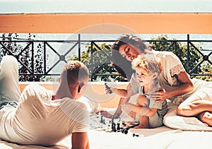 Young beautiful woman smiling to the boy who playing chess with his father.